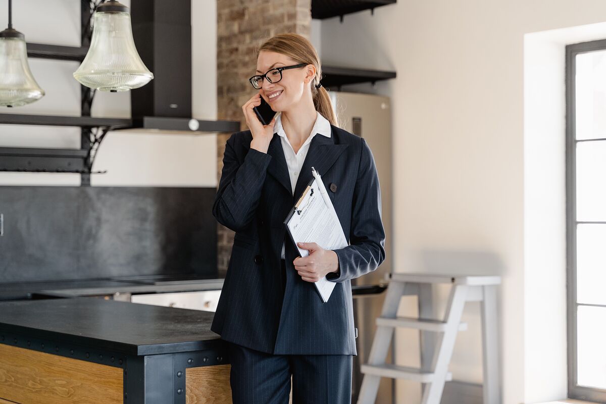 A real estate agent in a navy suit takes a phone call while holding a clipboard in the kitchen of a listed home