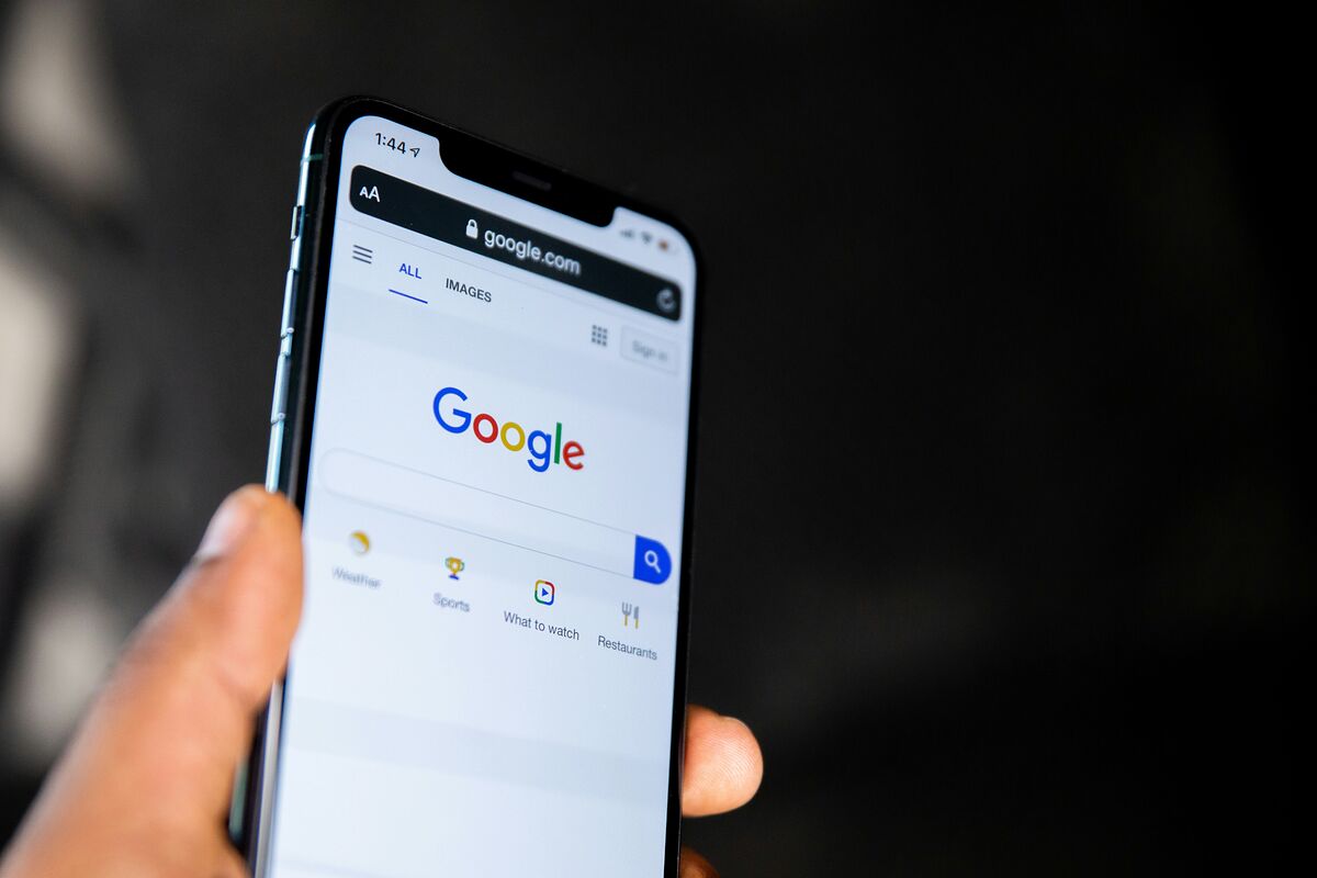 A hand holding a smartphone open on the Google search page, ready to search for a local real estate agent
